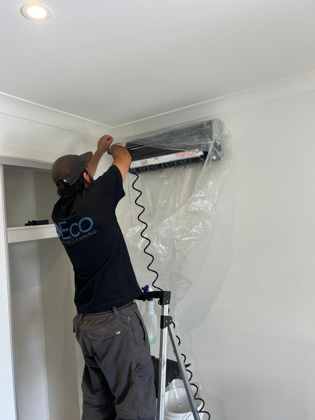Eco Aircon Cleaning technician cleaning a split system under a protective sheet